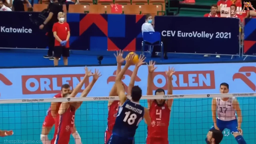 Volleyball hitter contacting the ball above a three-player block at the net